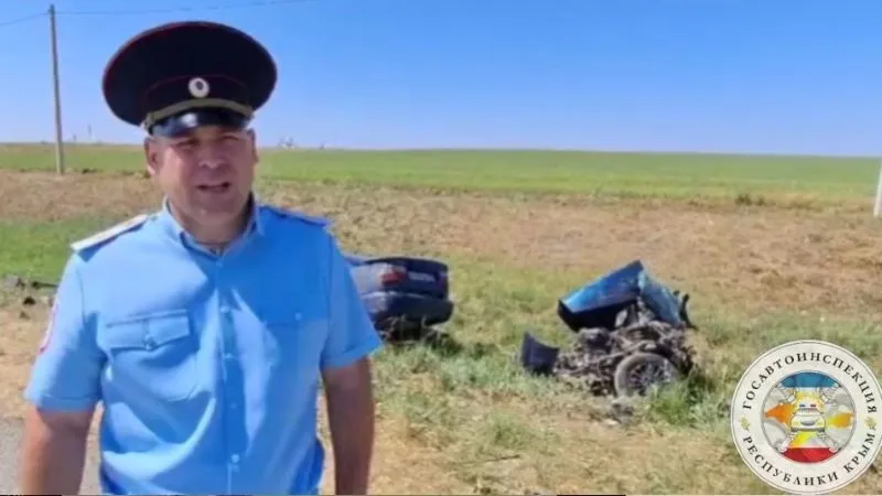 Позади сотрудника видны обломки автомобиля.